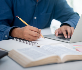 Person in front of a laptop taking notes in a notebook.
